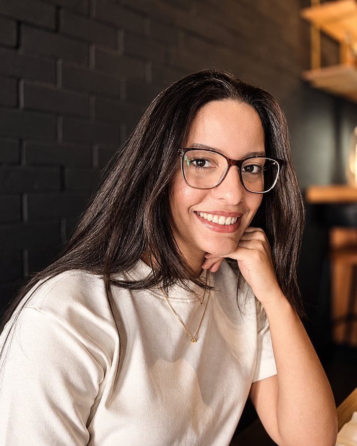 Susan Kelly sorrindo, com óculos de armação marrom e cabelo escuro e liso